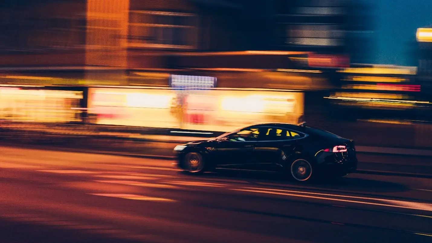 A blurred image of a black Tesla speeding at night, perhaps illustrating the consequences of a DWI arrest.