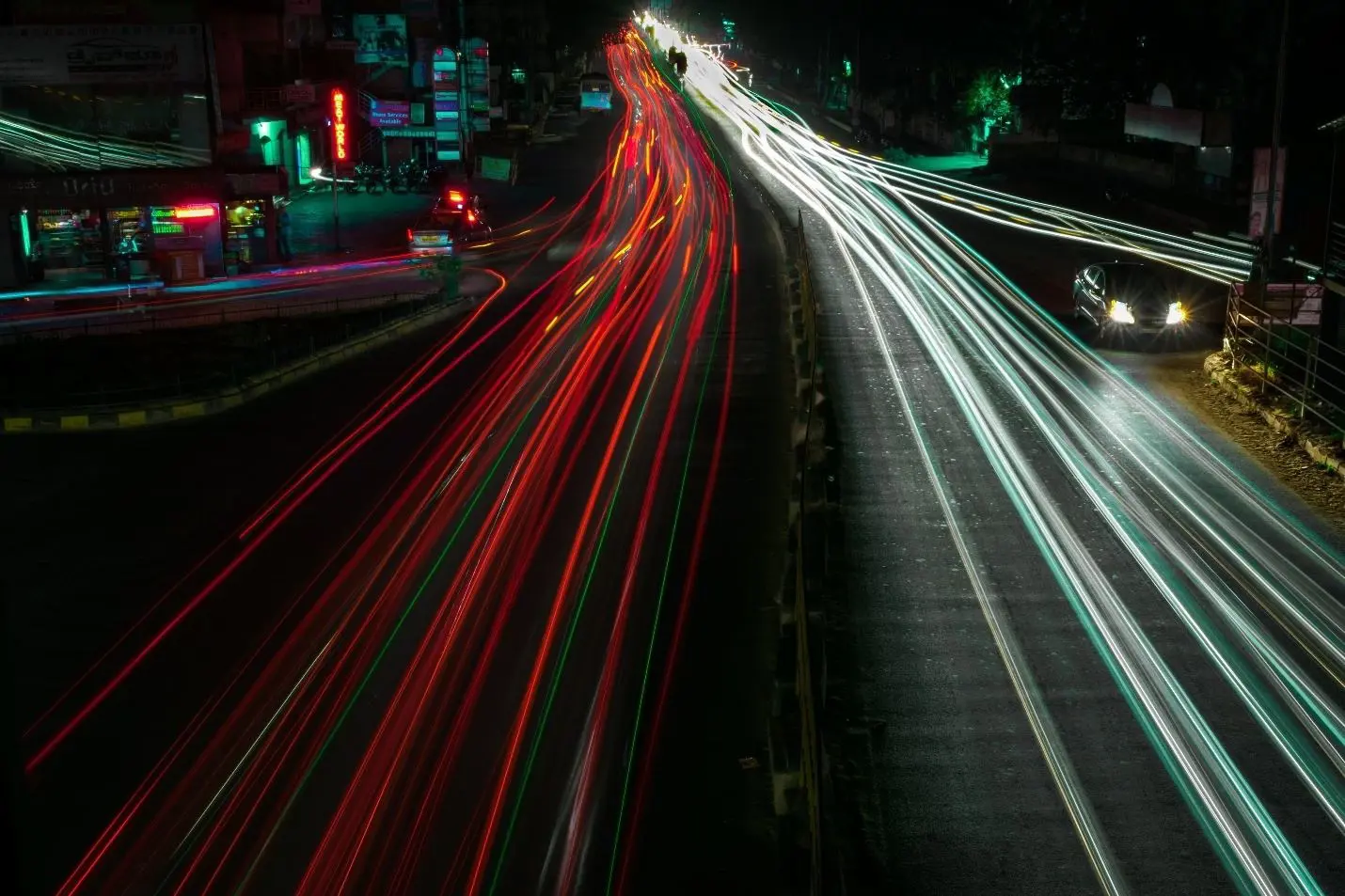 A street at night shows motion with light trails from cars passing in both directions.