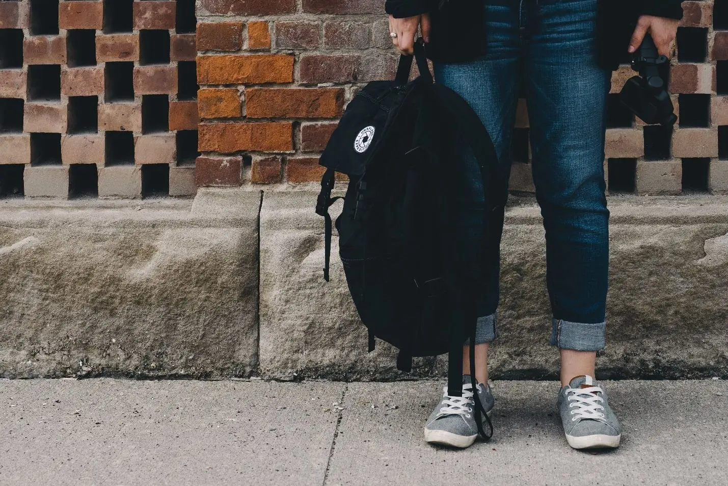 Person holding a black backpack stands outside a brick building.