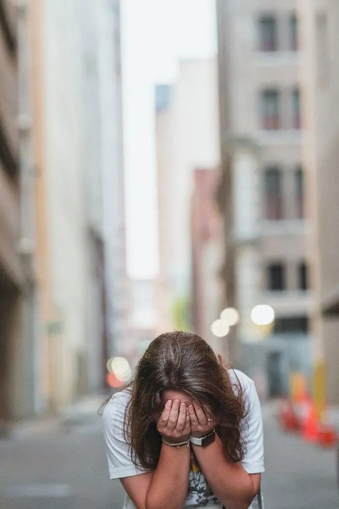 A person stands in an alleyway with their head in their hands. 